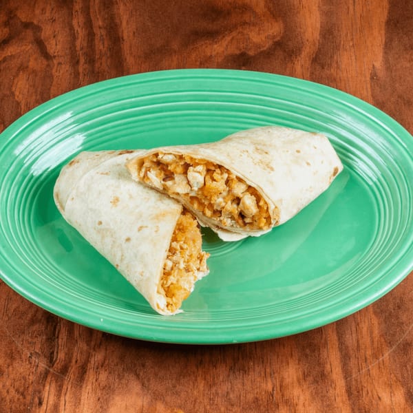 A chicken and rice burrito, cut in half, on a green plate with a wooden background.
