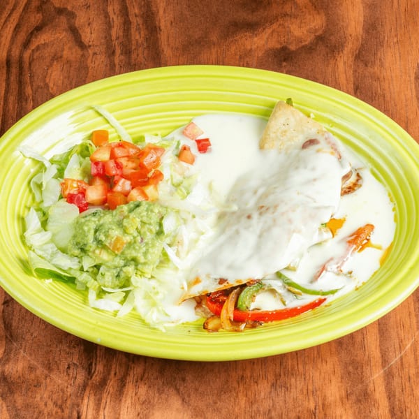 A quesadilla covered in white sauce, with lettuce, diced tomatoes, and guacamole on a lime green plate.