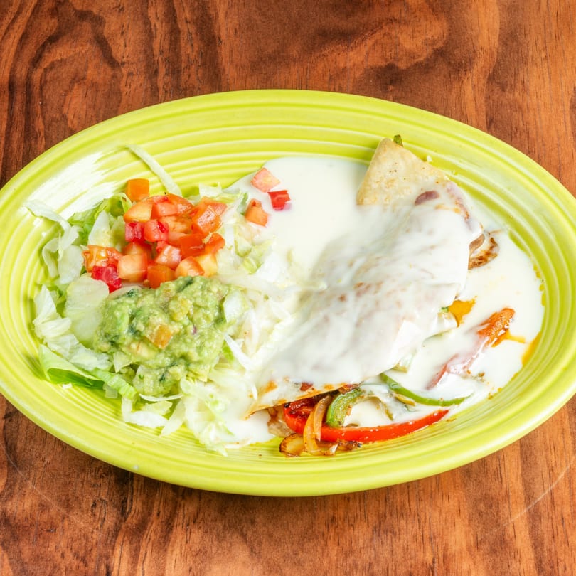A quesadilla covered in white sauce, with a side of lettuce, diced tomatoes, and guacamole.