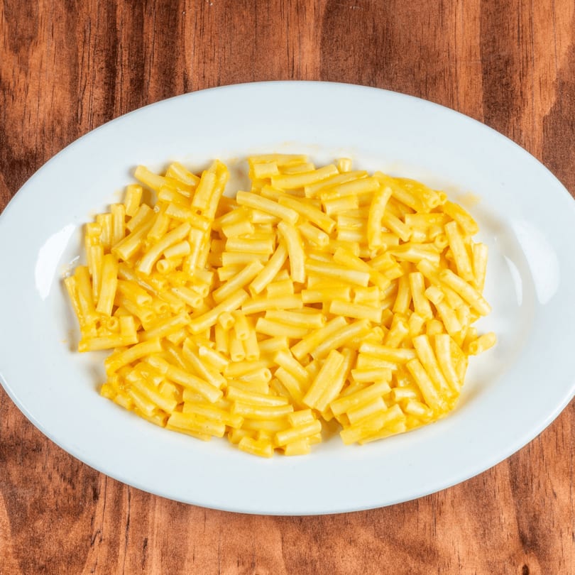 A white oval plate filled with creamy yellow macaroni and cheese on a wooden table.