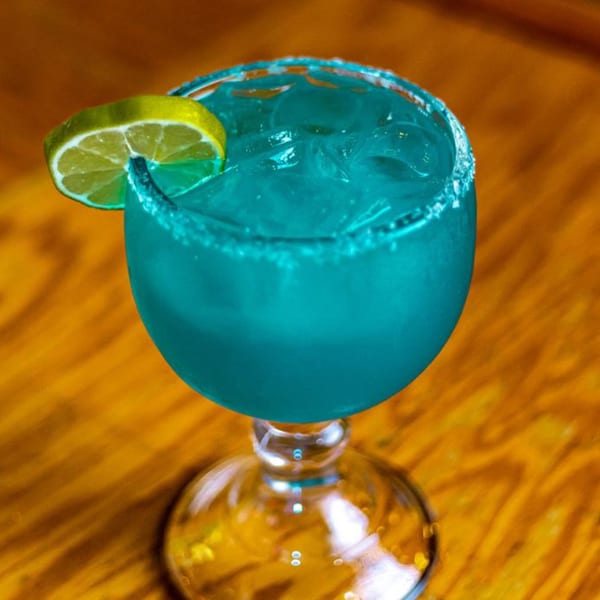 A vibrant blue margarita with ice, a salted rim, and a lime wedge on a wooden table.
