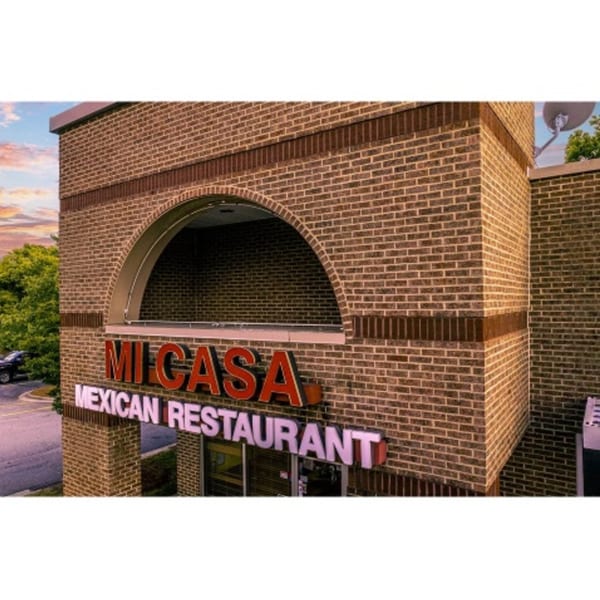 Exterior of Mi Casa Mexican Restaurant, a brick building with a large arched window and red signage.