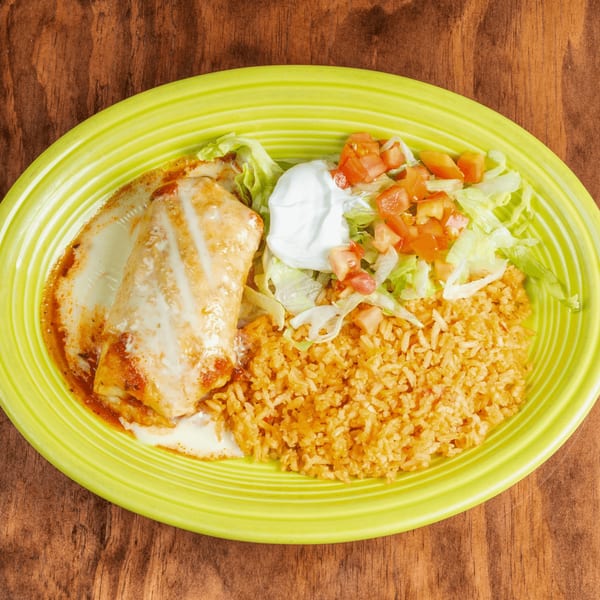 A burrito covered in white sauce and red sauce, with a side of rice, lettuce, tomatoes, and sour cream.
