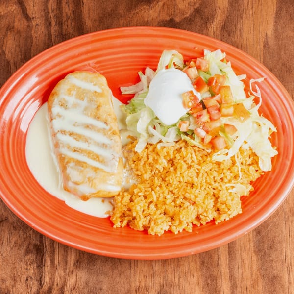 A golden-brown chimichanga drizzled with white sauce, served with rice, lettuce, tomatoes, and sour cream.