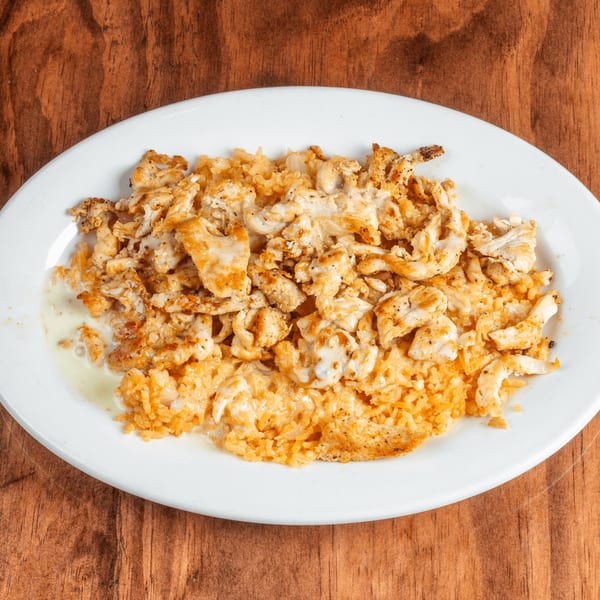 A white oval plate filled with seasoned chicken and rice, drizzled with a creamy white sauce.