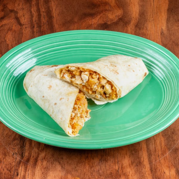 A chicken and rice burrito, cut in half, on a bright green plate against a wooden table.